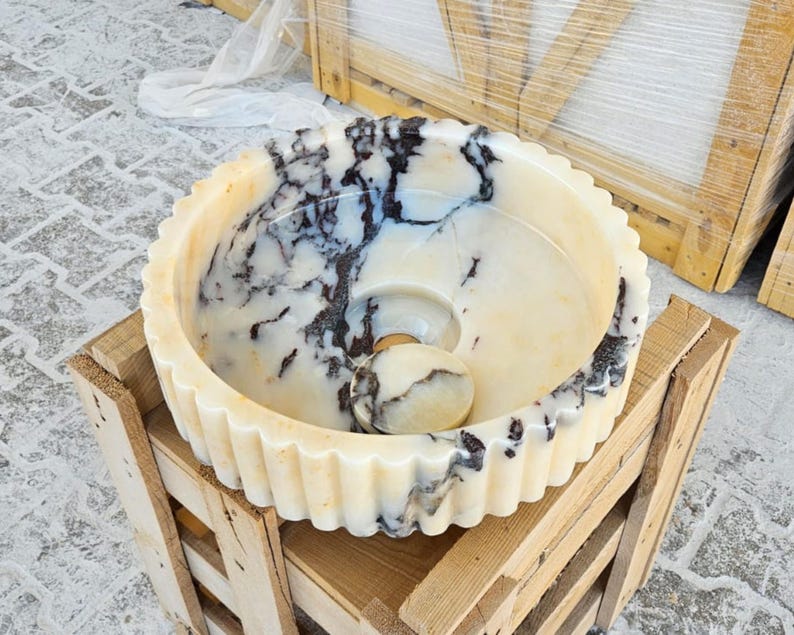 May include: A white marble sink with a fluted edge and a swirling black and white pattern. The sink is sitting on a wooden crate.