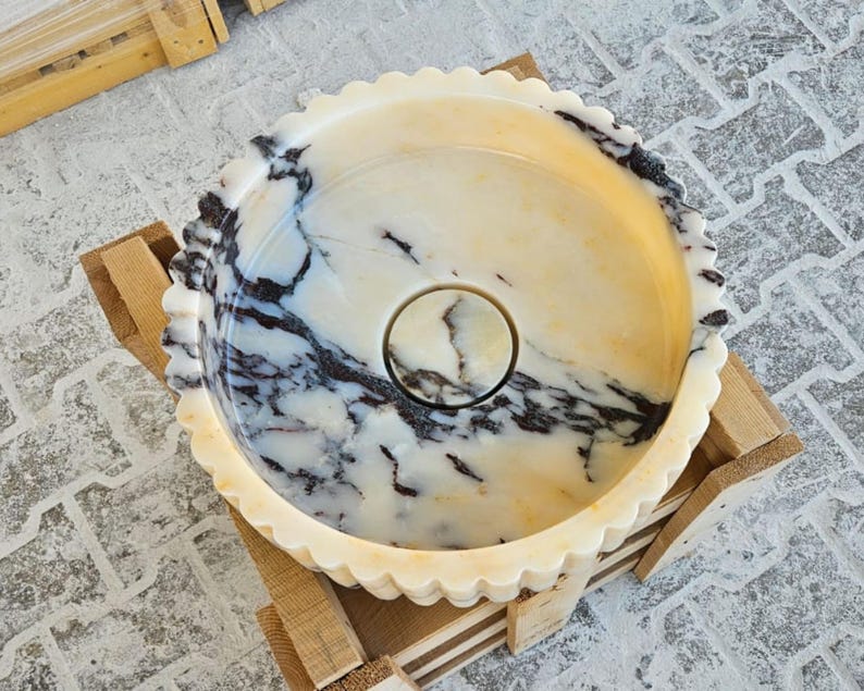 May include: A white marble bowl with black and brown veining. The bowl has a scalloped edge and a small hole in the centre.