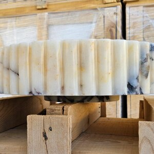 May include: A white marble sink with a fluted edge. The sink is sitting on a wooden pallet.
