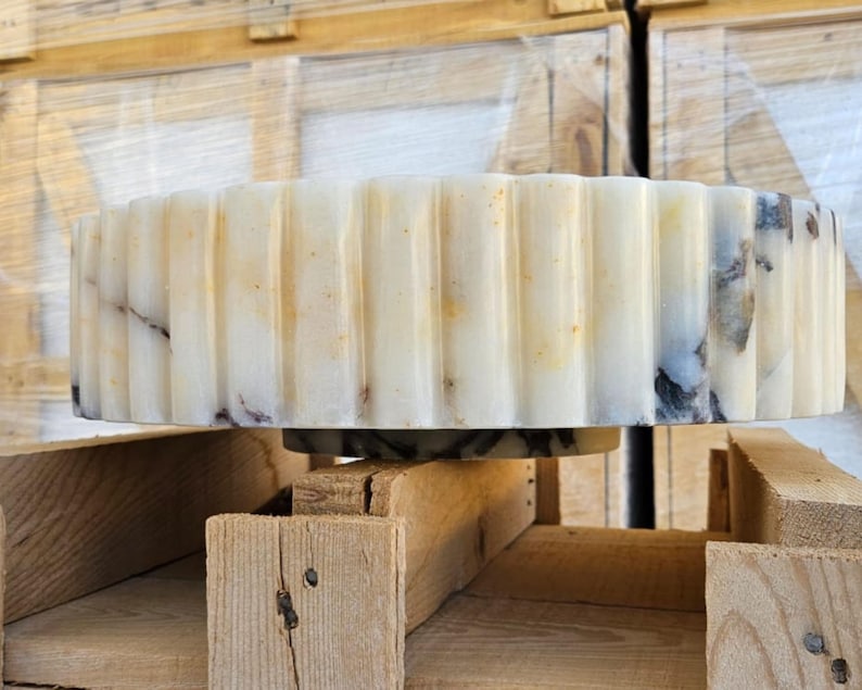 May include: A white marble sink with a fluted edge. The sink is sitting on a wooden pallet.