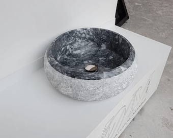 Può includere: Un lavandino rotondo in marmo grigio con un esterno testurizzato. Il lavandino ha un foro di scarico circolare al centro.