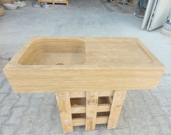 May include: A rectangular stone sink with a single basin and a draining board. The sink is made of travertine and has a light beige colour. The sink is sitting on a wooden pallet.