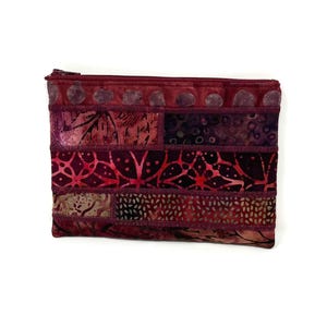 May include: A burgundy zippered pouch with a patchwork design of various shades of red and purple floral patterns. The pouch is made of fabric and has a zipper closure.