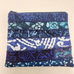 May include: A blue and white patchwork zippered pouch with a floral pattern. The pouch is made of fabric scraps sewn together.