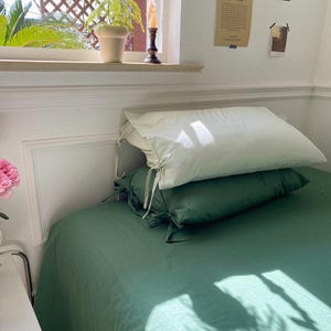 May include: A green bed with two pillows, one white and one green. The white pillow has ties on the corners. The bed is made with a green sheet and the pillows are on top of the sheet.