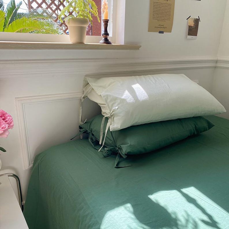 May include: A green bed with two pillows, one white and one green. The white pillow has ties on the corners. The bed is made with a green sheet and the pillows are on top of the sheet.