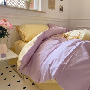 May include: A yellow and purple bedding set with a yellow pillow and a purple duvet cover. The bedding is made of soft, comfortable fabric and has a simple, elegant design.