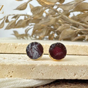 May include: A pair of gold stud earrings with round, dark red gemstone accents.