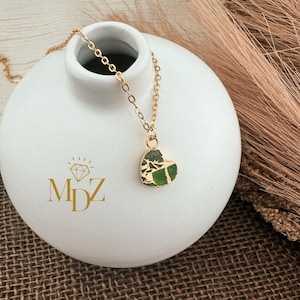 May include: A gold chain necklace with a green heart-shaped pendant. The pendant has a marbled pattern and is set against a white background.