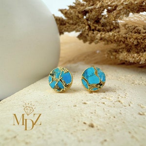 Op de afbeelding: Een paar gouden oorbel studs met turquoise en gouden inleg. De oorbellen zijn rond en hebben een uniek, marmerachtig patroon.