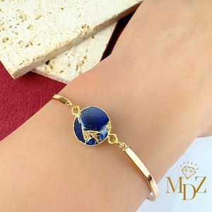 May include: Gold bracelet with a blue and gold circular stone charm. The stone has a marbled pattern.