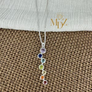 May include: A silver chain necklace with a pendant featuring seven round gemstones in a rainbow colour sequence. The gemstones are amethyst, sapphire, green, yellow, orange, and red.