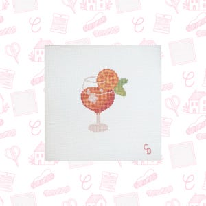 May include: A square white needlepoint canvas featuring a cross-stitch design of a stemmed glass filled with an orange-colored beverage, ice cubes, an orange slice garnish, and a green leaf. The letters CD are stitched in the bottom right corner.