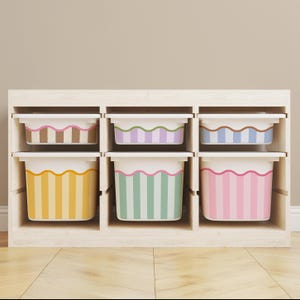 May include: A wooden storage unit with six cubbies, each holding a colorful bin. The bins feature striped patterns in various colors, including brown, purple, blue, yellow, green, and pink. The bins have white rims and are designed for organizing items.