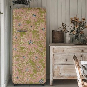 Op de afbeelding: Een koelkast in vintage stijl met een bloemenpatroon in roze en groene tinten. De koelkast staat in een keuken met een houten dressoir en een vaas met bloemen.