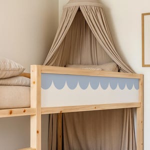 May include: A light wood bunk bed with a blue scalloped design on the headboard. The bed is adorned with beige bedding and a matching canopy. A framed botanical print hangs on the wall.