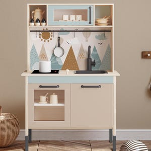 May include: A light blue and beige children's play kitchen with a black sink, a black stovetop, and a white cabinet with a glass door. The backsplash features a whimsical design of mountains, clouds, and a hot air balloon.