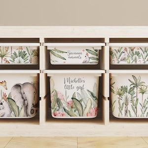 Puede incluir: Seis cestas de almacenamiento blancas con diseños de animales de la selva y flores. Las cestas están etiquetadas como "Savannah Animals", "Michelle's Little Girl" y tienen otros diseños de animales de la selva.