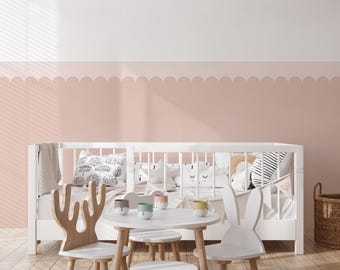 May include: A white crib with bedding and decorative pillows is in a room with a pink and white wall. A small white table with three stools and two wooden chairs are in front of the crib. A woven basket is on the right.