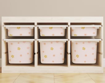 May include: Six white storage bins with pink and gold floral patterns are stacked in a wooden shelf unit. The bins are all the same size and are arranged in two rows of three.