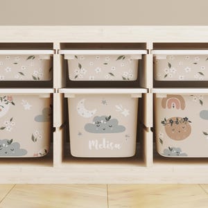 May include: A set of six beige storage bins with different whimsical designs, including clouds, moons, and flowers. The bins are labeled with the name "Melissa".