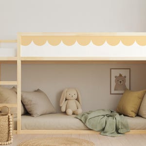 May include: A light wood bunk bed with a scalloped yellow and white design. The lower bunk has a beige mattress, pillows, and a green blanket. A stuffed bunny and a framed bear print are also visible.