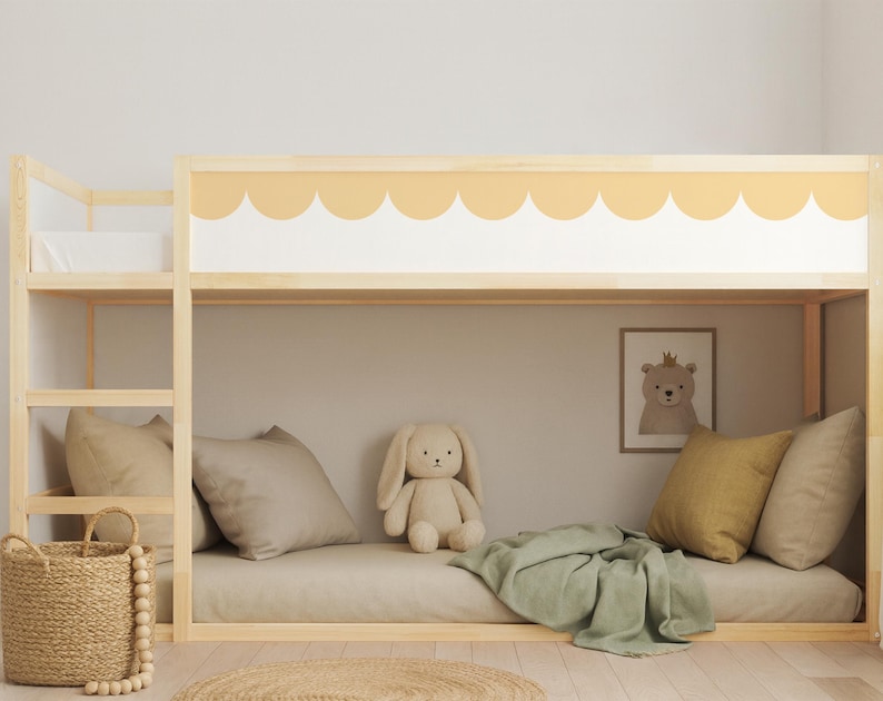 May include: A light wood bunk bed with a scalloped yellow and white design. The lower bunk has a beige mattress, pillows, and a green blanket. A stuffed bunny and a framed bear print are also visible.