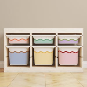 May include: A light-coloured wooden storage unit featuring six rectangular bins arranged in two rows. Each bin is white with a distinct coloured wavy line accent, including orange, green, purple, brown, yellow, and red, providing organised storage.