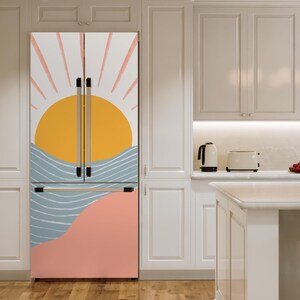 May include: A white refrigerator with a removable door cover featuring a stylised sunset design with pink, yellow, blue and white colours. The design includes a sun, waves and a pink and peach coloured landscape.