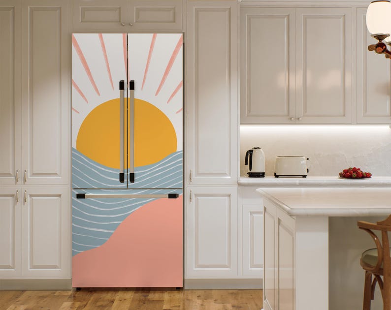 May include: A white refrigerator with a removable door cover featuring a stylised sunset design with pink, yellow, blue and white colours. The design includes a sun, waves and a pink and peach coloured landscape.