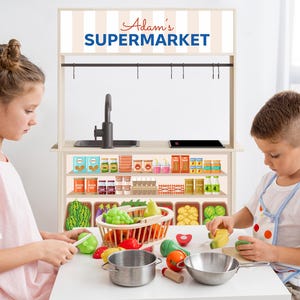 May include: Two children playing with a wooden toy supermarket playset. The set features a counter with shelves stocked with toy food, a sink, and a sign that reads "Adam's Supermarket".