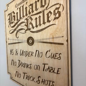 May include: Wooden sign with the text "Considine's Billiard Rules" in a decorative font. The sign includes rules such as "No Cues" and "No Drinks on Table." A pool ball and cues are also depicted.