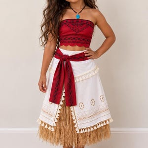 Peut inclure: Un ensemble deux pièces composé d'un haut court rouge sans bretelles avec des motifs tribaux noirs et un ourlet festonné, associé à une jupe portefeuille blanche avec une ceinture rouge, des franges crème et une base en raphia beige.