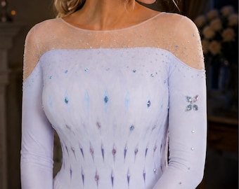 May include: A light blue and white gown with long sleeves and a sheer neckline. The bodice features a pattern of diamond-shaped embellishments in shades of blue and purple. The sleeves and neckline are adorned with sparkling crystals.