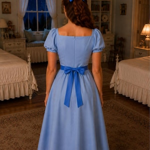 May include: A light blue dress with a square neckline and short, puffed sleeves. The dress features a matching bow at the waist and a bow in the hair. The dress has a flared skirt and is made of a soft fabric. The dress is a classic, vintage style.
