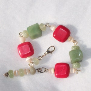 May include: A green and red gemstone bracelet with a gold clasp. The bracelet features square-shaped green and red stones, as well as smaller white stones.
