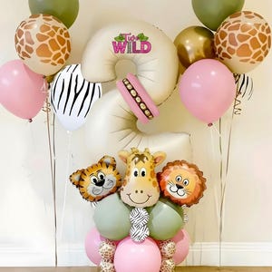 Może przedstawiać: Świąteczna aranżacja balonowa z motywem safari. Zawiera balony w kształcie zwierząt, różowe i zielone balony oraz balony z nadrukami żyrafy i zebry. Układ wymawia "Two Wild".