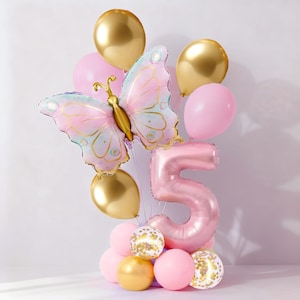 Könnte beinhalten: Eine festliche Ballonanordnung mit einem großen schmetterlingsförmigen Ballon mit rosa und blauen Flügeln, einem Ballon mit der Zahl 5 und mehreren goldenen und rosa Ballons. Einige Ballons haben Konfetti. Perfekt für eine Geburtstagsfeier.