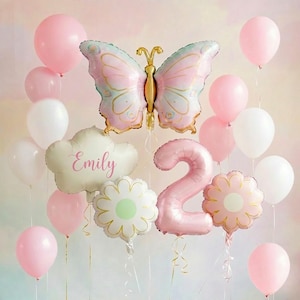 May include: A collection of pink and white balloons, including a large butterfly-shaped balloon with gold accents. Other balloons include a cloud-shaped balloon with the name "Emily" and a number "2" balloon, plus flower-shaped balloons.