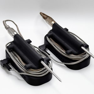 May include: Two black holders for meat thermometers. Each holder has a black plastic base with a slot for the thermometer probe and a coiled wire. The probes are silver and extend out from the holders.