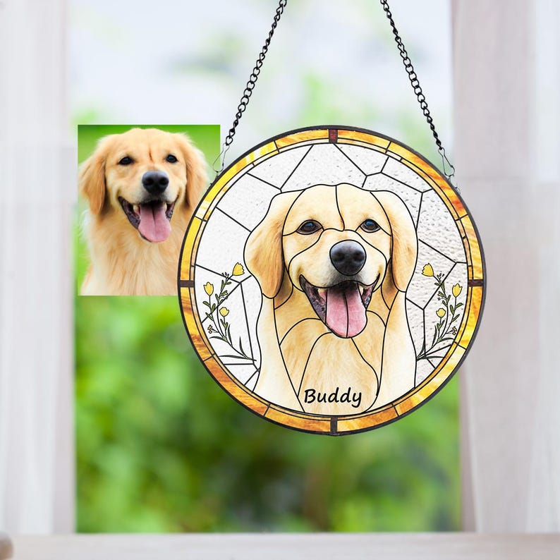 May include: A round stained glass window featuring a smiling golden retriever dog with the name "Buddy" below. The window is framed in gold and hangs from a black chain. A smaller photo of the dog is to the left.