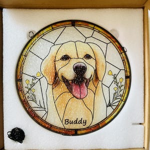 May include: Round stained glass window featuring a smiling golden retriever dog with the name "Buddy" at the bottom. The dog is in shades of tan and white, with a pink tongue. The window has a yellow and brown border.