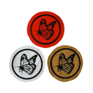 May include: Three round fabric patches with a black butterfly design. The patches are red, white, and brown.