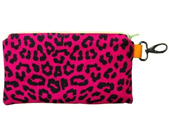 May include: A pink zippered pouch with a black leopard print design. The pouch has a lime green zipper and an orange strap with a silver clip.