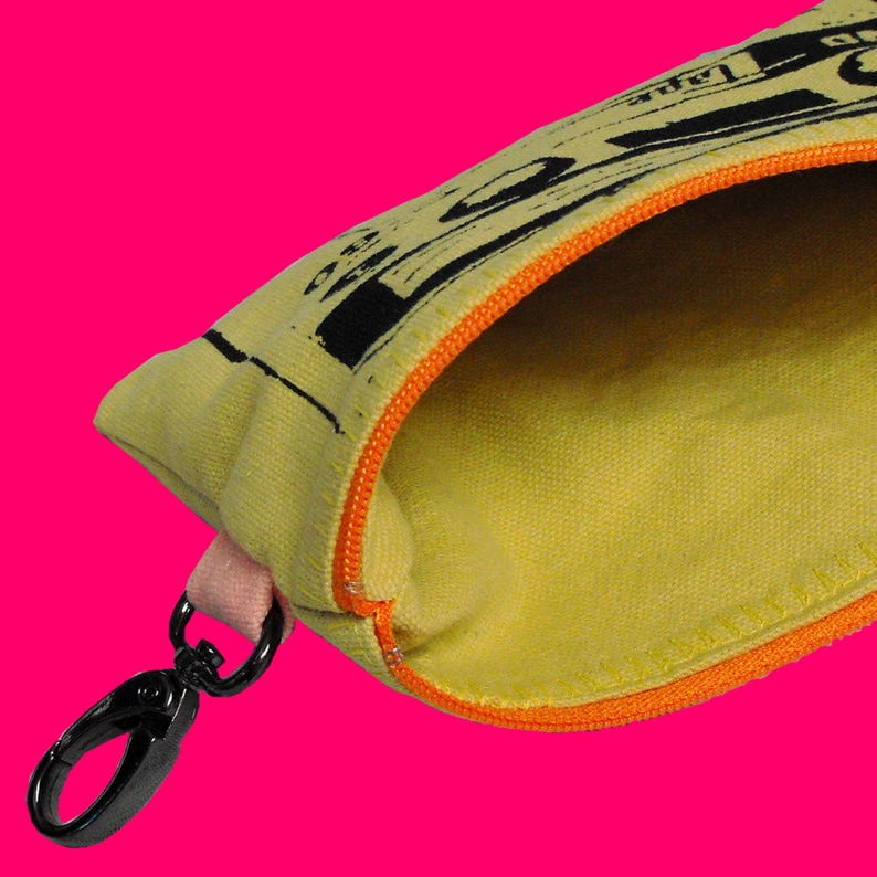May include: A yellow canvas zippered pouch with an orange zipper and a black metal clip. The pouch has a black and white print of a cassette tape on the front.