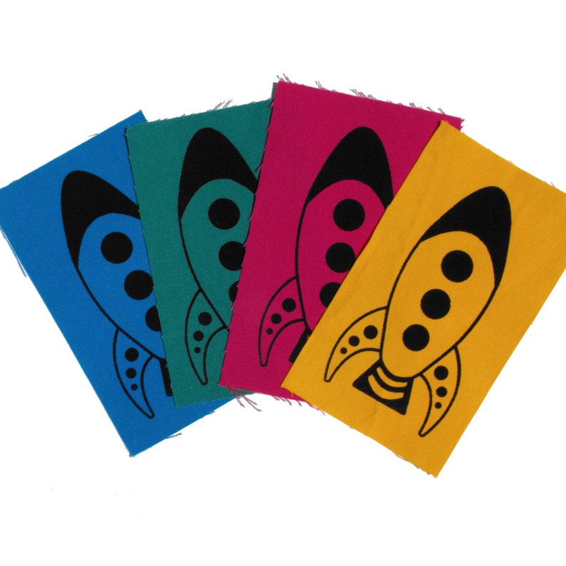 May include: Four fabric patches featuring a black rocket ship design. The patches are in blue, teal, pink, and yellow.