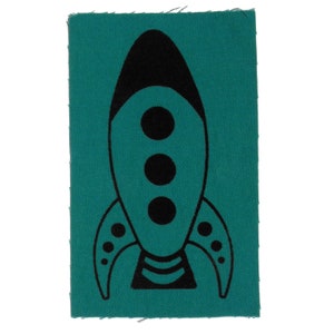 May include: A teal blue fabric patch with a black rocket ship design. The rocket ship has three black circles in the centre and a black outline.