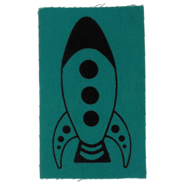 May include: A teal blue fabric patch with a black rocket ship design. The rocket ship has three black circles in the centre and a black outline.