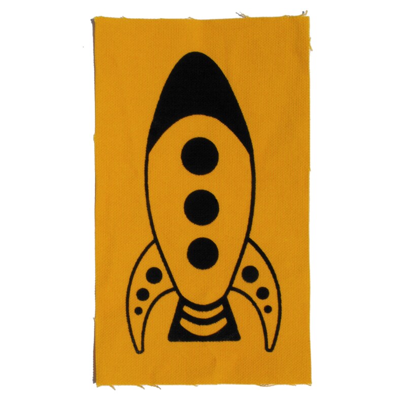 May include: A yellow fabric patch with a black rocket ship design. The rocket ship has three black circles in the centre and a black stripe at the bottom.