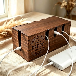 Könnte beinhalten: Eine rechteckige Kabelmanagement-Box aus dunkelbraunem Holz mit Deckel. Die Vorderseite zeigt ein lasergraviertes kreisförmiges Design mit dem Text "WORLD'S BEST DADDY" und dem Namen "Jarrett" darunter, ergänzt durch Hammer- und Schraubenschlüssel-Symbole.